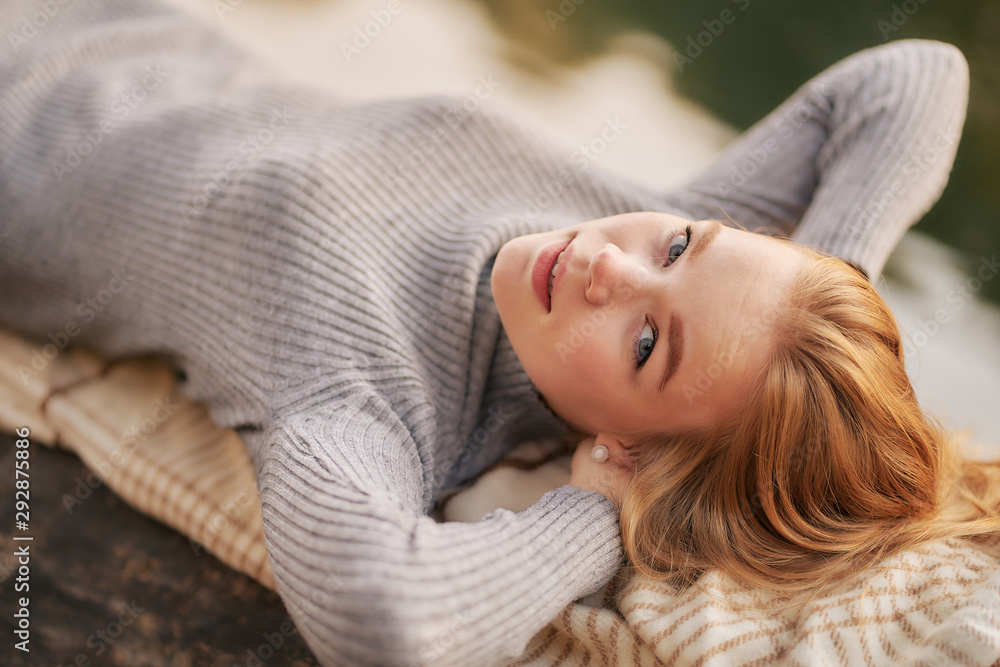 red-haired young woman in a park in golden autumn. in a gray dress lies on a log against the background of the river red-haired young woman in a park in golden autumn. in a gray dress lies on a log against the background of the river