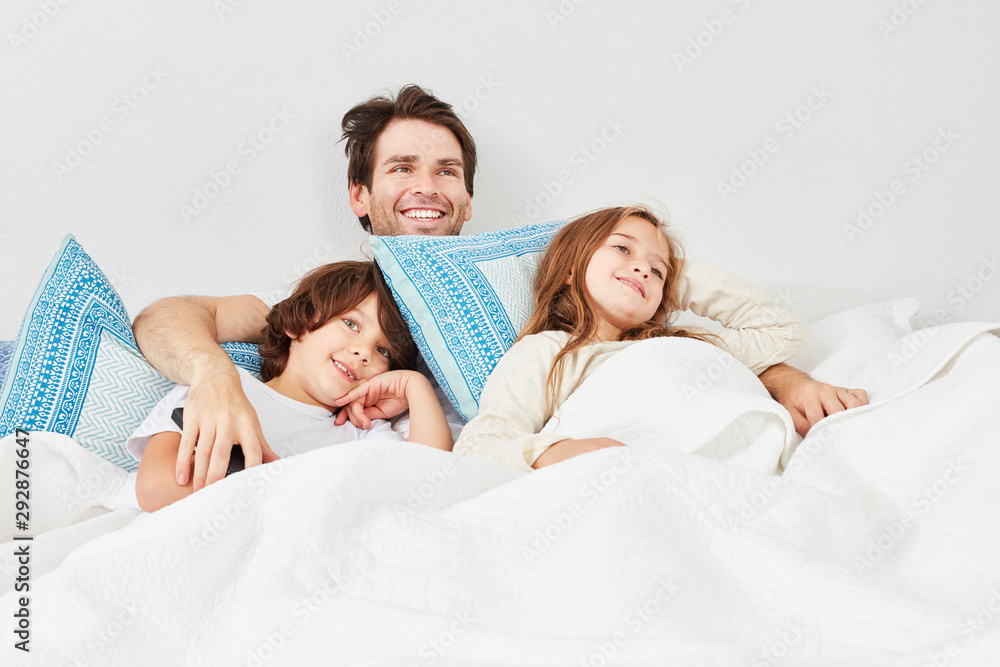 Fototapeta premium Vater und Kinder im Bett schauen Fernsehen