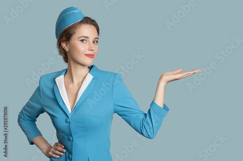 Beautiful stewardess holding blank on her hand. Blue background.