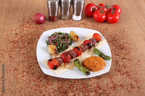 Meat & Tomato Kebabs with Fresh Pepper and Vegetables on a Wooden Table Filled with Turkish Spices