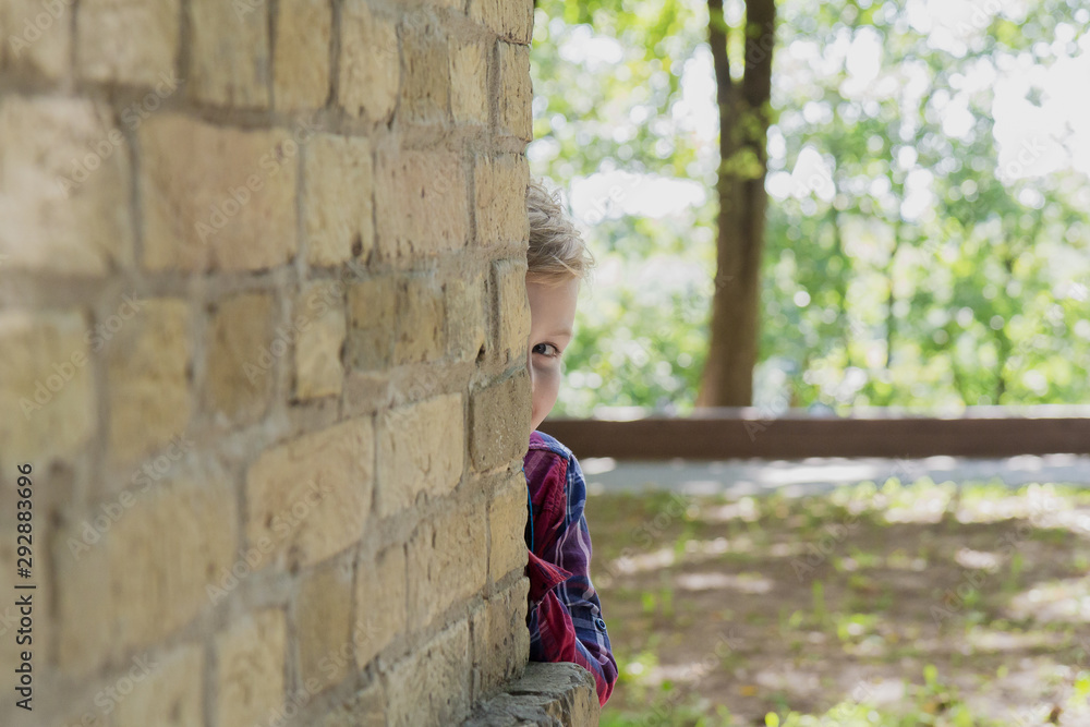 Little boy peeks out from behind a wall in a park. Little boy peeks out from behind a wall in a park.