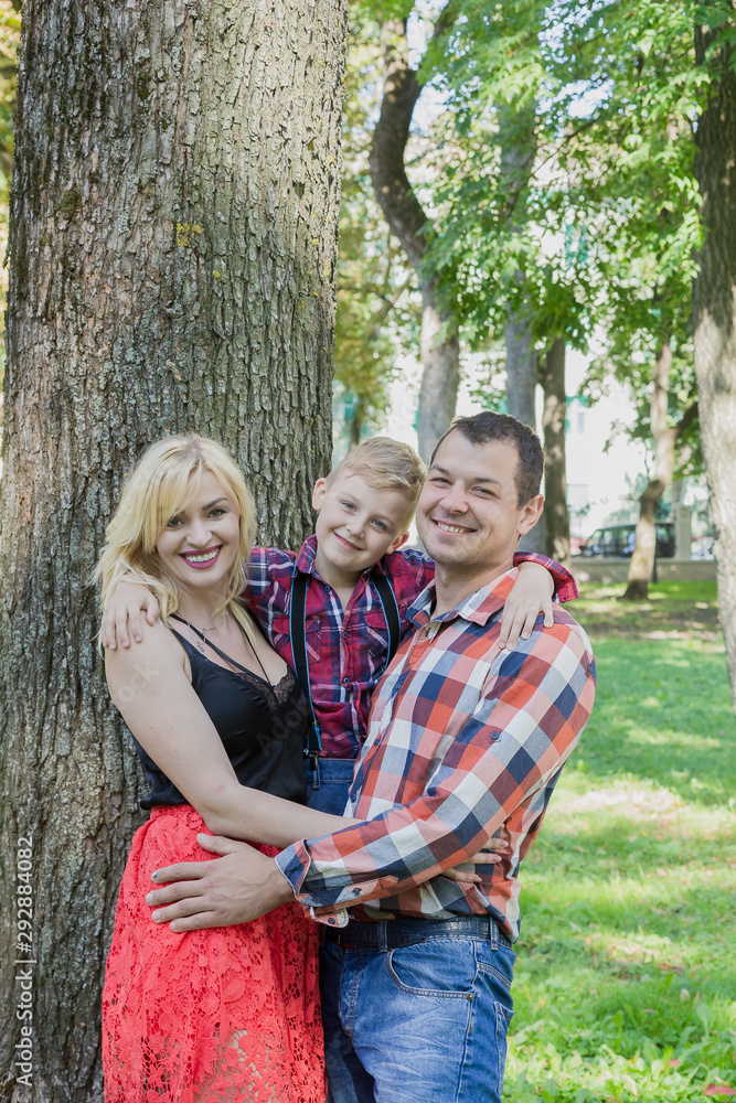 Beautiful happy young family hugs by a tree in the park.