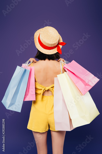 back view of girl in straw hat with shopping bags isolated on purple