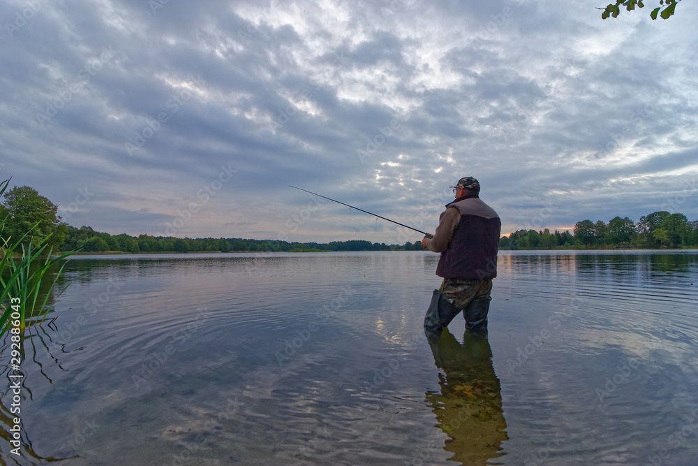 fisherman catching fish on spinning in lake during cloudy day fisherman catching fish on spinning in lake during cloudy day