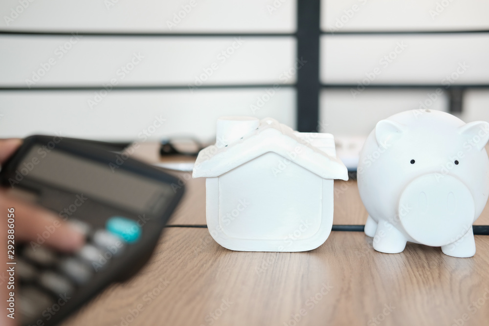 hand calculating with calculator. house model piggy bank on desk. saving money for buying house property. real estate investment hand calculating with calculator. house model piggy bank on desk. saving money for buying house property. real estate investment