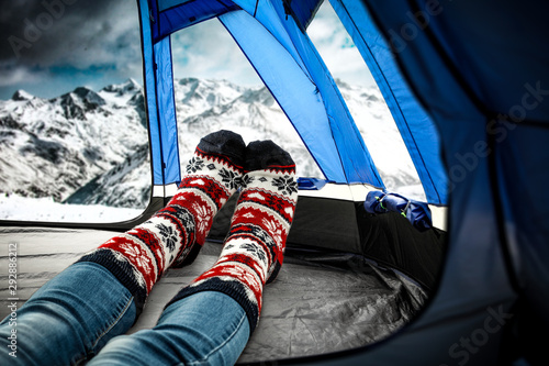 Woman legs with winter socks and tent with mountains landscape 