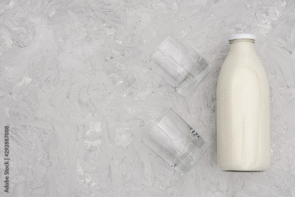 Milk in glass bottle and two empty glasses on gray background with copy space. Flat lay top view Milk in glass bottle and two empty glasses on gray background with copy space. Flat lay top view