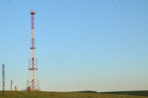 Communications tower at the blue sky background and green meadow