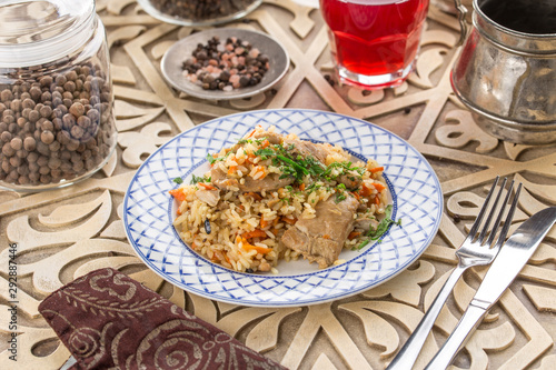 pilaf with chicken on white plate and glass of red drink on oriental wooden table