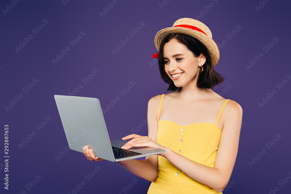 smiling girl in straw hat using laptop isolated on purple smiling girl in straw hat using laptop isolated on purple