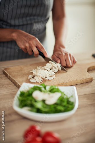 Close up of mixed race woman in apron standing in kitchen and chopping mushrooms.