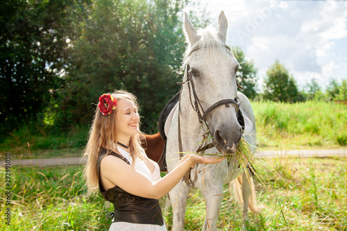 Beautiful caucasian young girl walking with a horse and enjoys summertime in countryside.