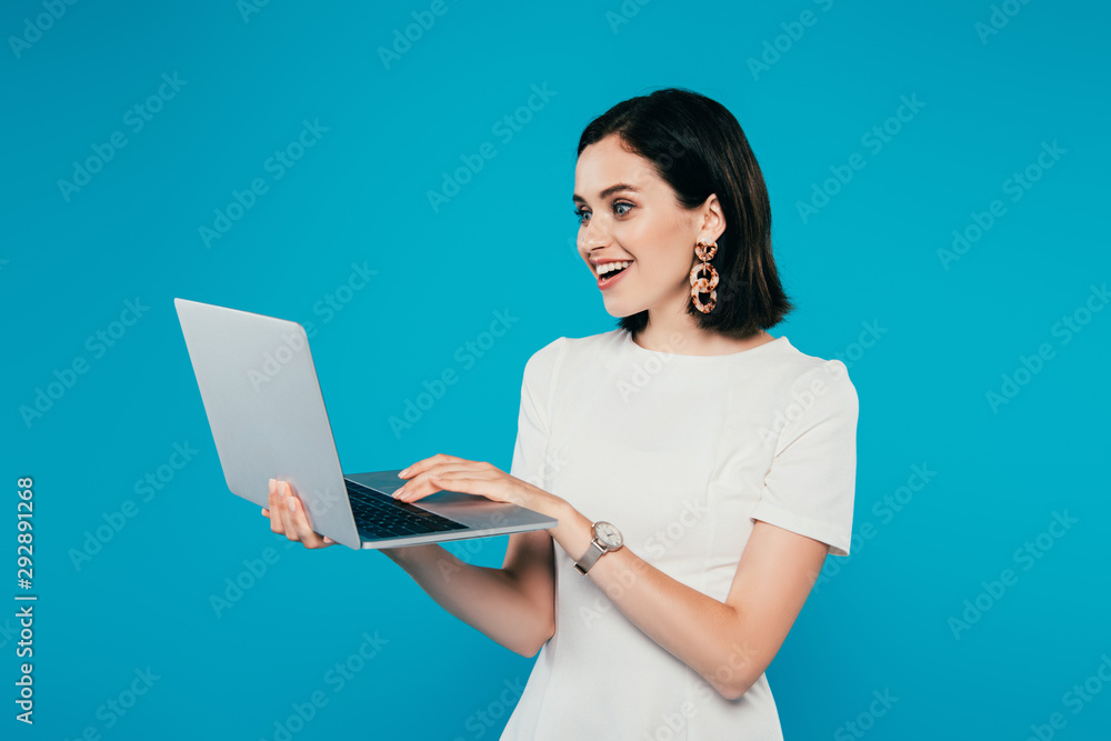 excited smiling elegant woman using laptop isolated on blue excited smiling elegant woman using laptop isolated on blue