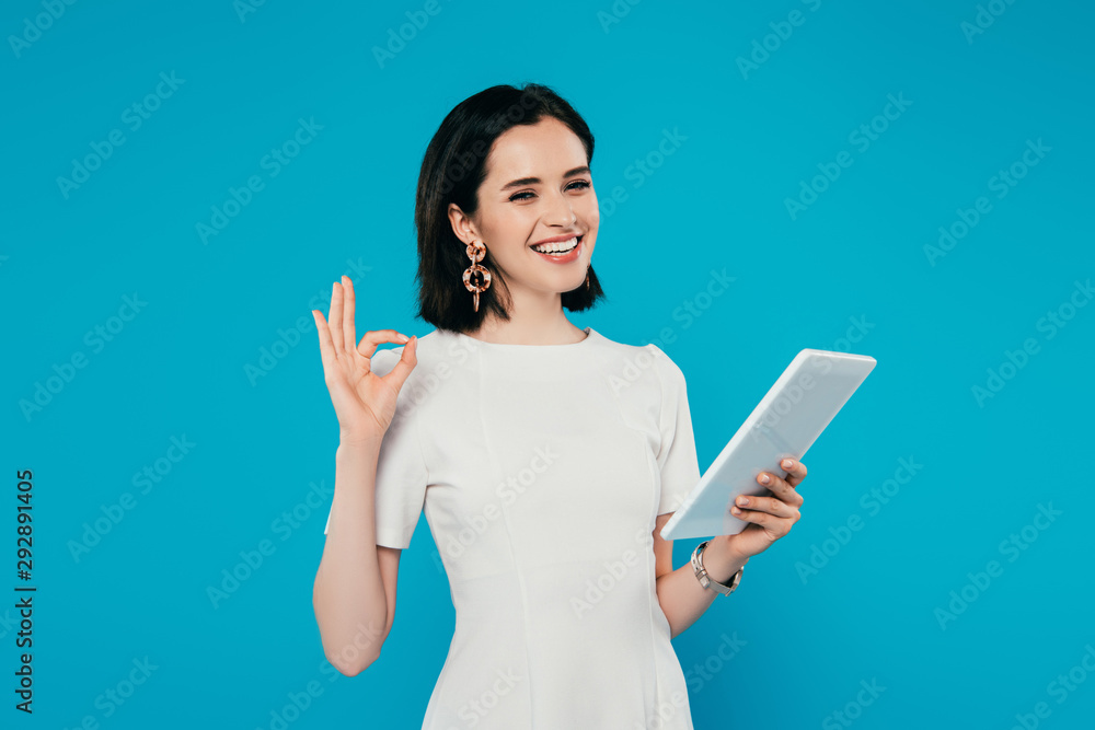 smiling elegant woman holding digital tablet and showing okay sign isolated on blue smiling elegant woman holding digital tablet and showing okay sign isolated on blue