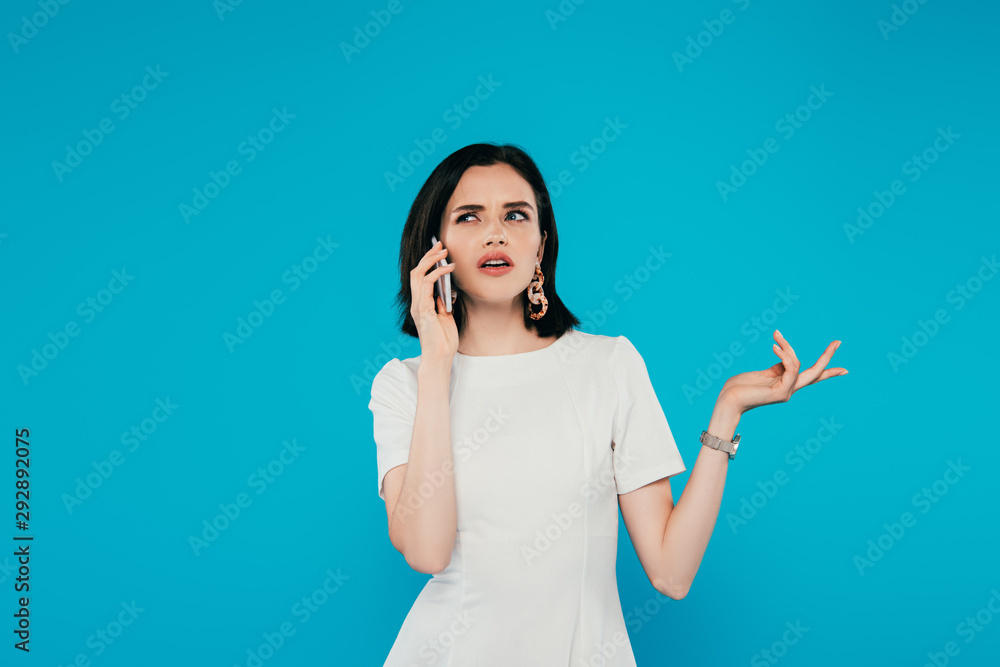 displeased elegant woman in dress talking on smartphone and gesturing isolated on blue displeased elegant woman in dress talking on smartphone and gesturing isolated on blue