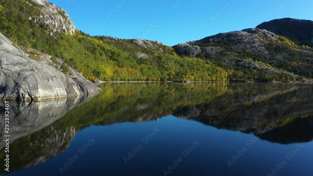 Aerial drone push in shot over a calm lake, water surface as reflecting back the landscape, perfect mirror image of mountains and autumn forest on a sunny day. Aerial drone push in shot over a calm lake, water surface as reflecting back the landscape, perfect mirror image of mountains and autumn forest on a sunny day.