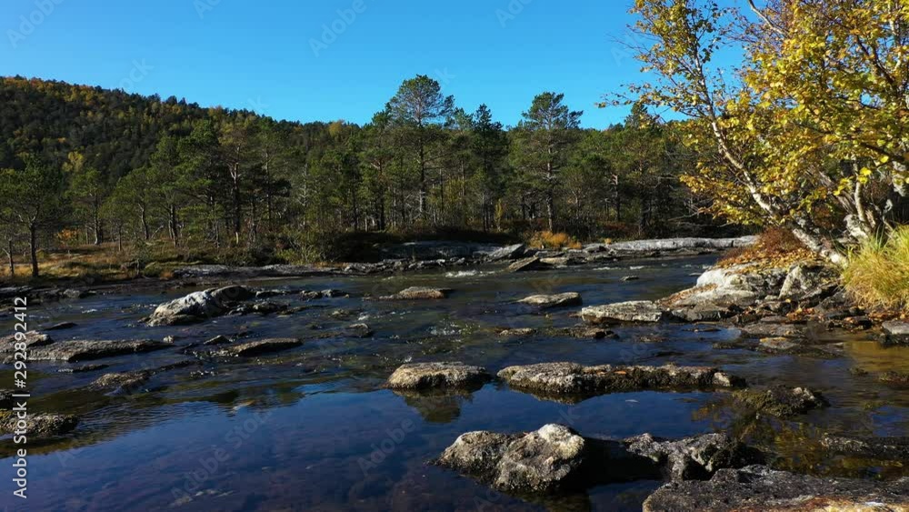 Stabile low angle shot of a river with rocks and stones in it surrounded a forest in the mountains on a bright autumn day. Stabile low angle shot of a river with rocks and stones in it surrounded a forest in the mountains on a bright autumn day.