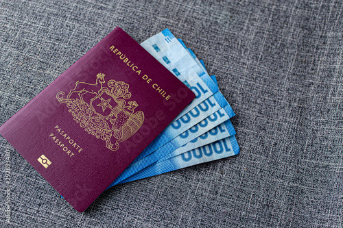 One Red Chilean passport with  and some Pesos Chilenos on a gray fabric desk
