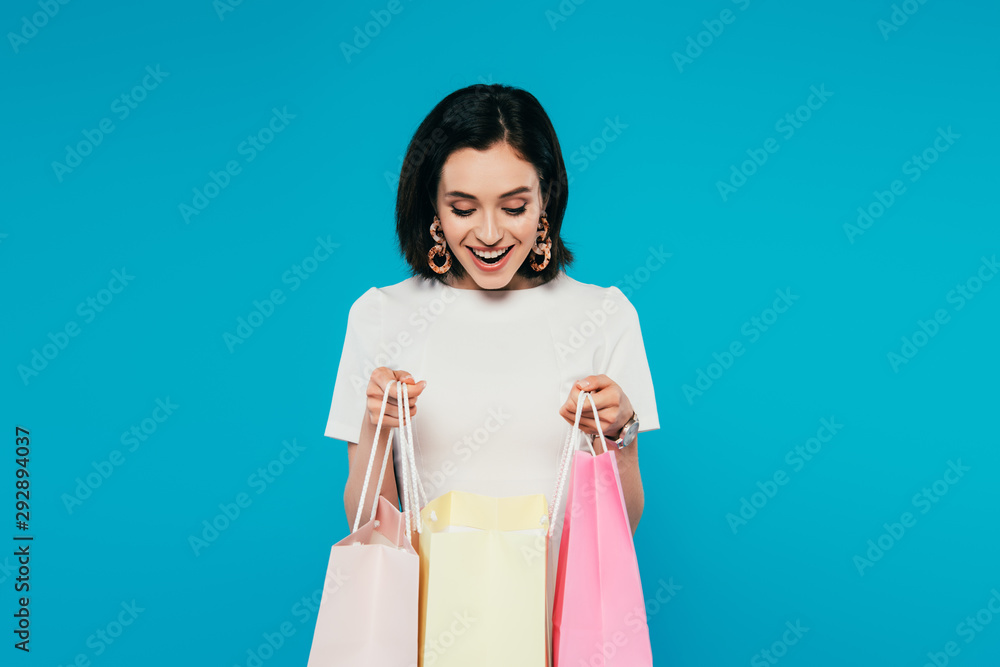 excited elegant woman in dress holding shopping bags isolated on blue excited elegant woman in dress holding shopping bags isolated on blue