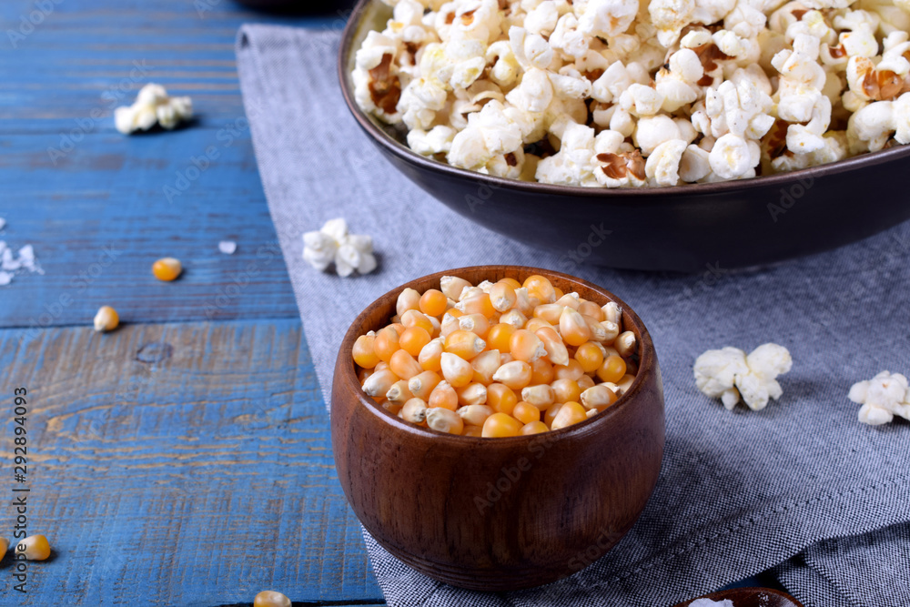 Unpopped corn kernels for making popcorn in a wooden cup on blue table Unpopped corn kernels for making popcorn in a wooden cup on blue table