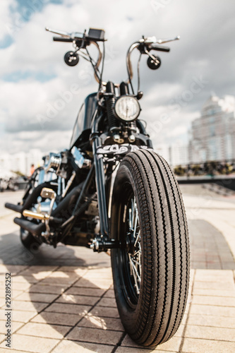 The front wheel of the motorcycle with a drum brake and a cable to it is the front fork with a shock absorber and a spring on a homemade motorcycle in a vintage style