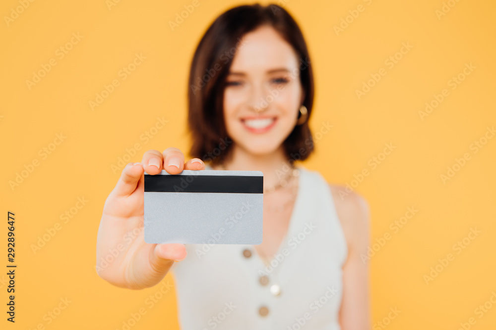 selective focus of smiling elegant girl holding credit card isolated on yellow