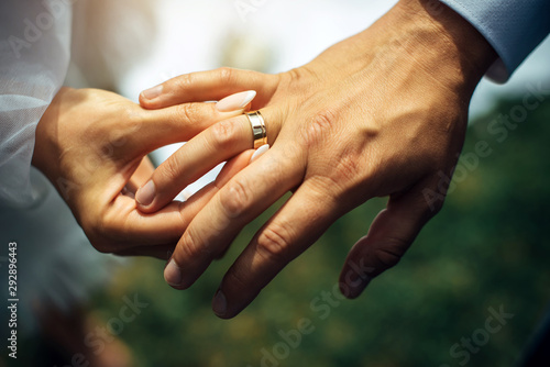 Young bride put a gold wedding ring on the groom's finger, close-up. Wedding ceremony, exchange of rings. On the hand of man wearing a wedding ring.