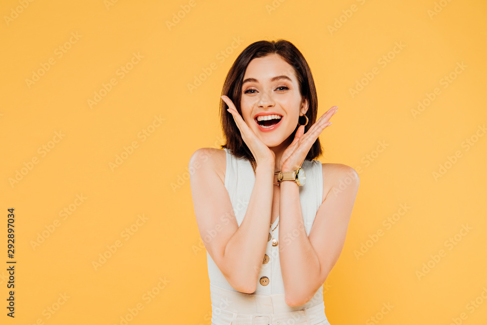 Fototapeta premium excited smiling elegant girl with hands near face isolated on yellow
