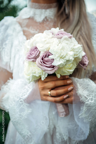 Hands of young bride holding beautiful wedding bouquet. Bride's hand with a wedding ring on her finger. Bride in vintage white dress holds a bouquet of roses.