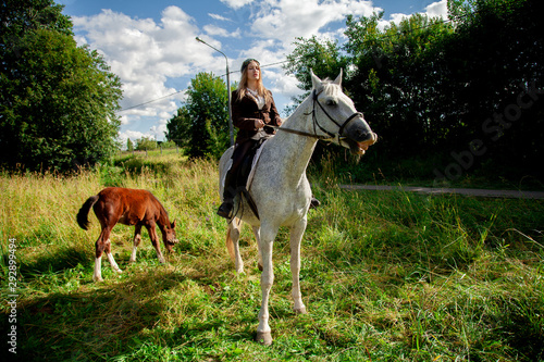 Beautiful caucasian young girl walking with a horse and enjoys summertime in countryside. © goldeneden
