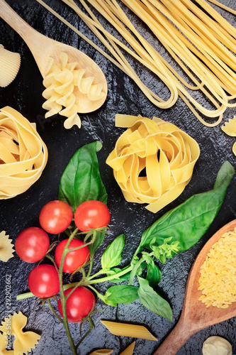 Italian pasta on a black background. Spaghetti, pappardelle, orzo, farfalle and other types, with tomatoes and basil