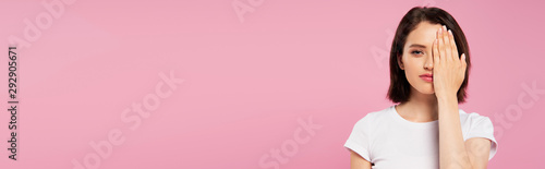 panoramic shot of beautiful girl covering face with hand isolated on pink
