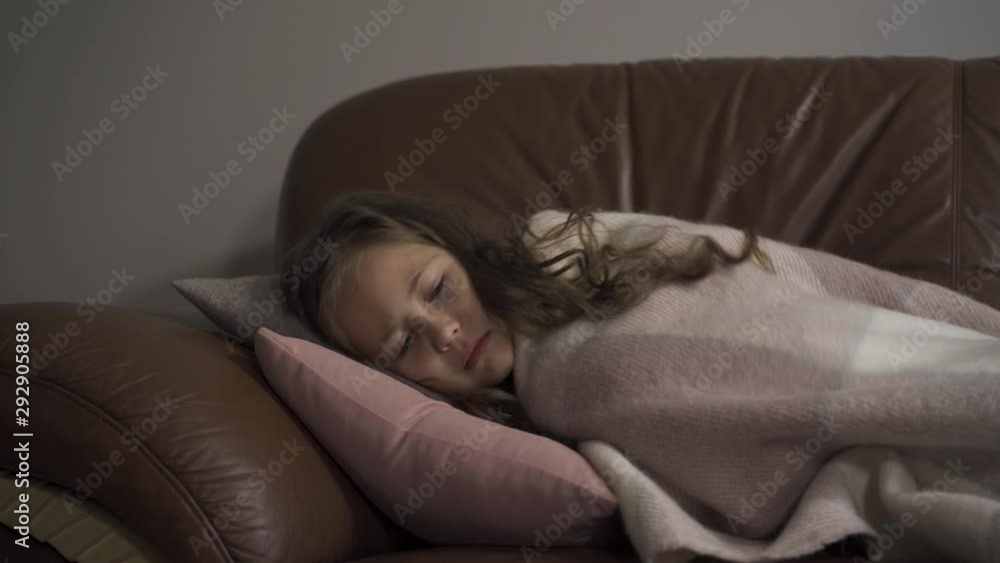 Sick young caucasian girl coughing while lying under blanket at home. The child has fever. Concept of health, illness, sickness, common cold, treatment Sick young caucasian girl coughing while lying under blanket at home. The child has fever. Concept of health, illness, sickness, common cold, treatment