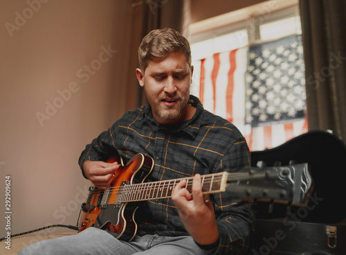Canvas Print Handsome american man playing acoustic guitar and singing with passion at home