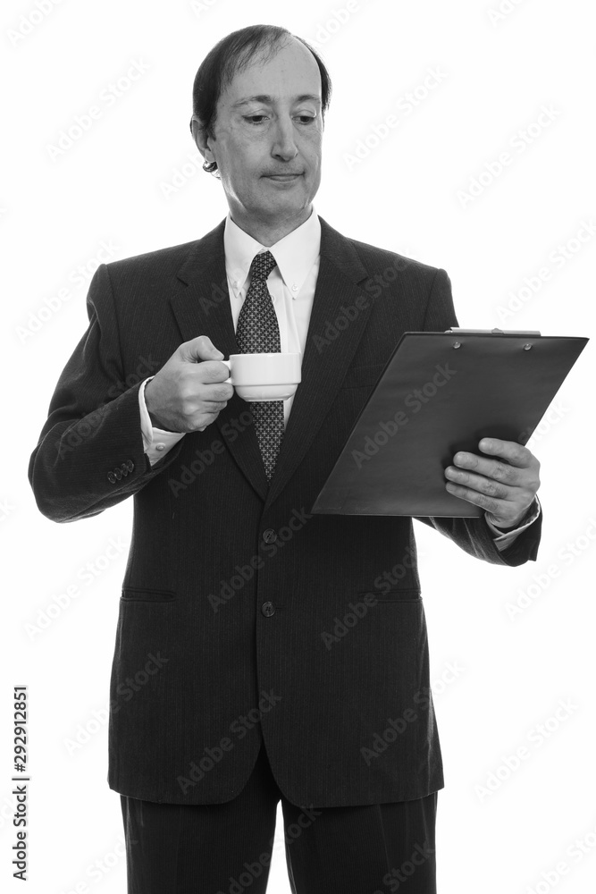 Studio shot of mature businessman holding coffee cup while reading on clipboard Studio shot of mature businessman holding coffee cup while reading on clipboard