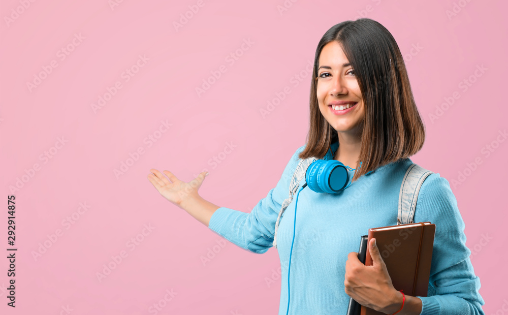 Young student girl with blue sweater and headphones pointing back with the index finger presenting a product on pink background Young student girl with blue sweater and headphones pointing back with the index finger presenting a product on pink background