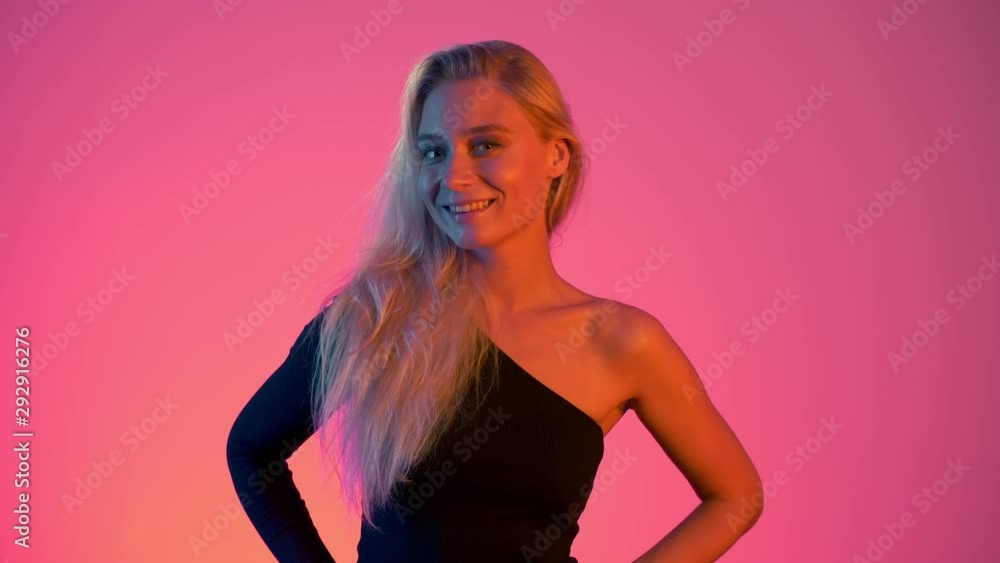 Neon lights concept. Young blond woman winks to camera flirting on gradient pink background. Happy girl smiles in studio in vivid red and blue colors Neon lights concept. Young blond woman winks to camera flirting on gradient pink background. Happy girl smiles in studio in vivid red and blue colors