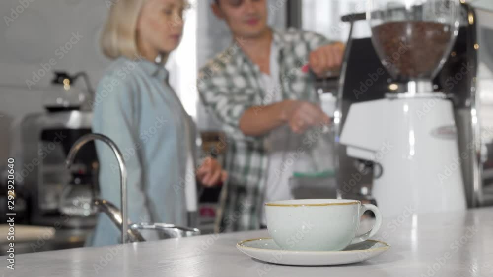 Selective focus on a coffee cup two baristas working on background. Coffee shop workers using coffee machine, preparing drinks for customers. Employment, lifestyle concept Selective focus on a coffee cup two baristas working on background. Coffee shop workers using coffee machine, preparing drinks for customers. Employment, lifestyle concept