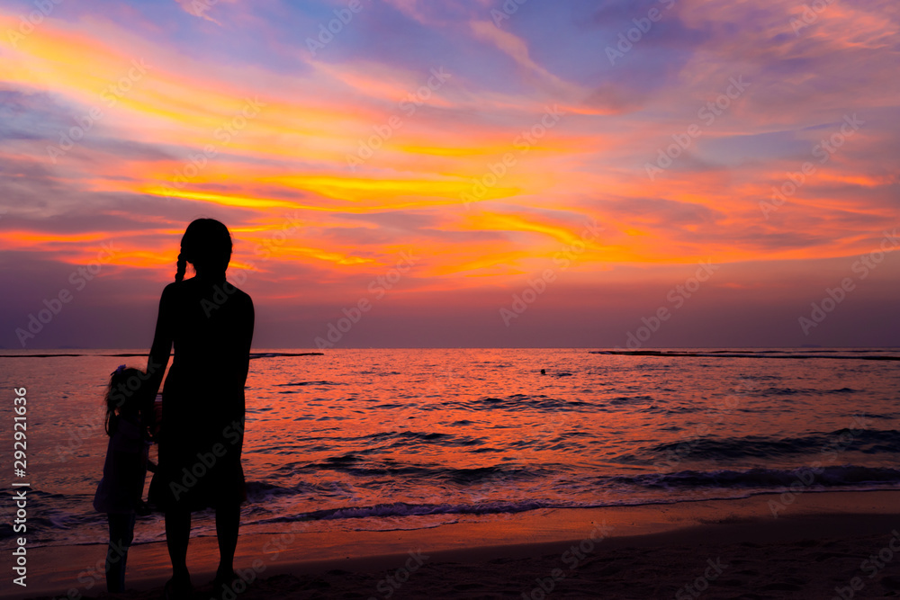Silhouette girl with younger sister stand on the beach with twilight colorful sky on sea in sunset or sunrise time