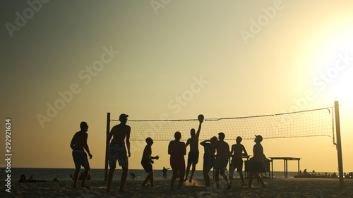 People play volleyball on the beach at sunset. Friends playing volleyball on a beach during sunset. Summer vacation concept.