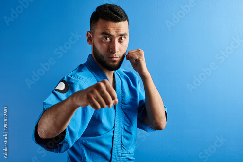 Asian Kazakh karate fighter in kimono uniform is combat on blue background with copy space isolated