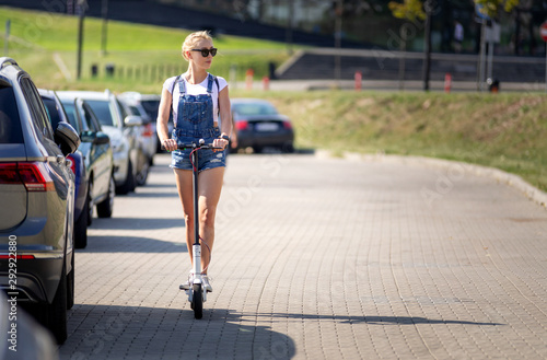 Full length shot woman riding an electric scooter in the street between cars