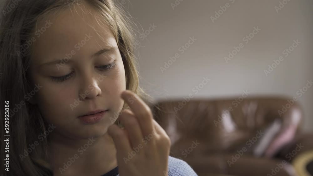 Close-up of sick little girl in blue sweater examining the green pill. Caucasian child undergoing treatment at home. Close-up of sick little girl in blue sweater examining the green pill. Caucasian child undergoing treatment at home.