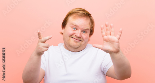 young big size man smiling and looking friendly, showing number eight or eighth with hand forward, counting down against pink wall photo