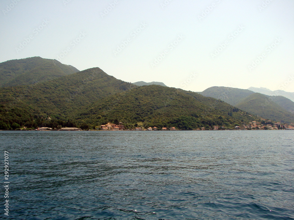 The beauty of the Montenegrin hills is covered with dense green forest reflected on the water surface of the azure bay.