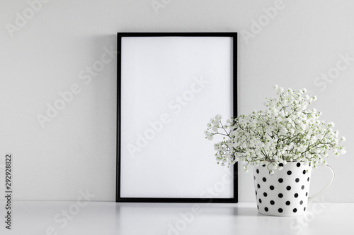 Black frame photo on white wood table and small white flowers in vase. White gypsophila flowers on shelf or desk. Mock up with decor elements.