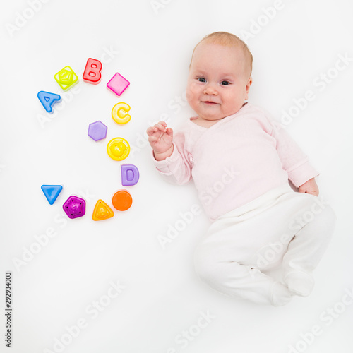 Portrait of a sweet infant baby girl wearing a red dress and bonnet, isolated on white in studio with number tree from toys, cubes, letters and molds