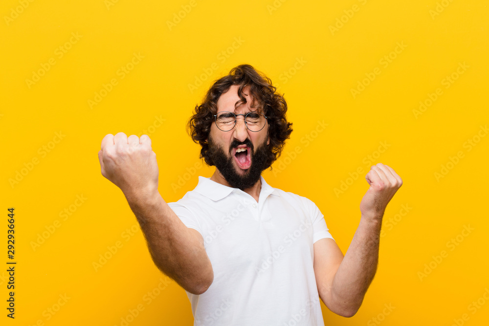 young crazy man shouting triumphantly, looking like excited, happy and surprised winner, celebrating against yellow wall - obrazy, fototapety, plakaty 