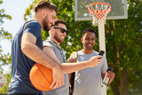 sport, leisure games and male friendship concept - group of men or friends with smartphone on outdoor basketball playground