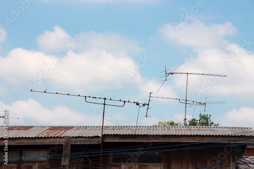 The old Television antenna on the house roof has a blue sky.